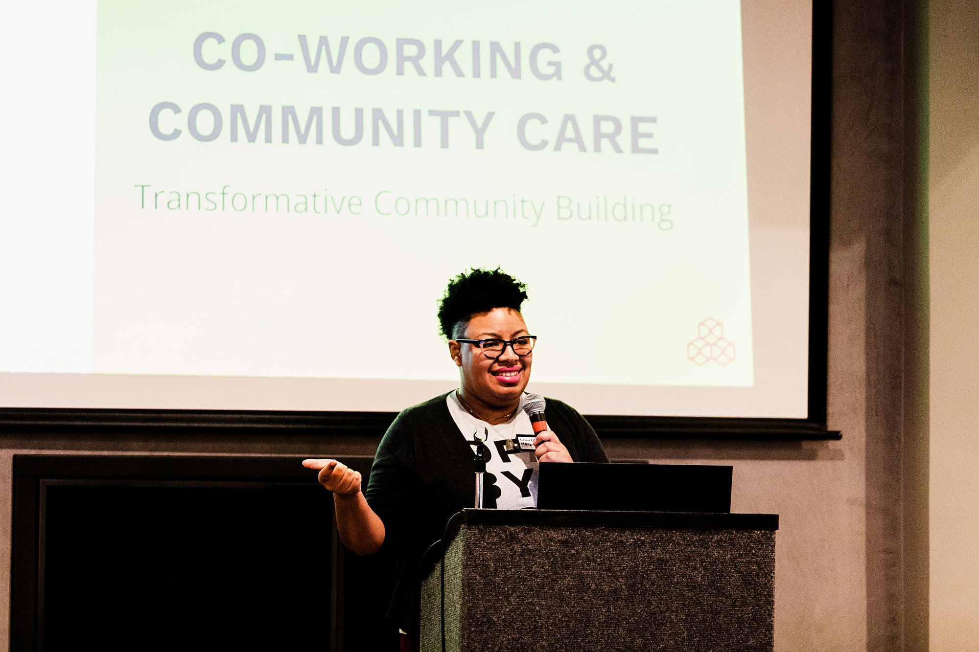CEO Courtney Harge in front of a screen that reads Co-Working & Community Care